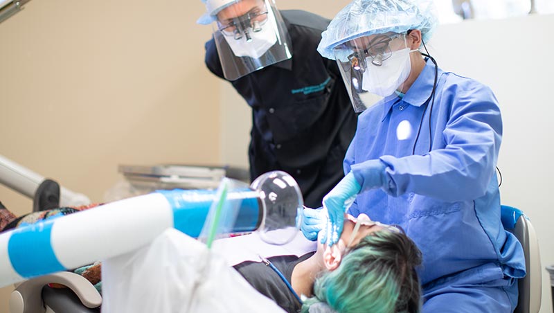 A dental hygiene trainee works on a patient