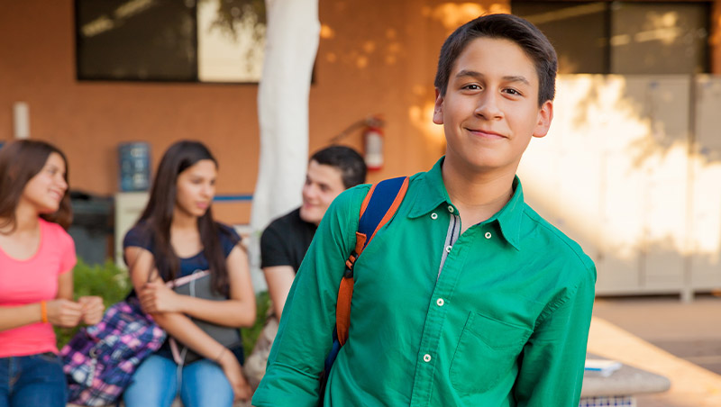 A young student with a book bag stands in front of his peers