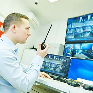 A corporate security guard watches monitors and uses a hand radio
