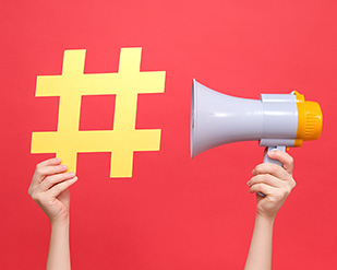 Closeup of a hand holding a megaphone next to a hashtag symbol