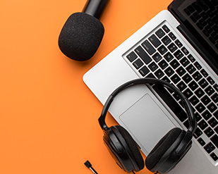 A laptop, headphones, headphone adapter and microphone sit on an orange background