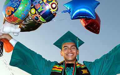 An MVC graduate celebrates in regalia while holding balloons