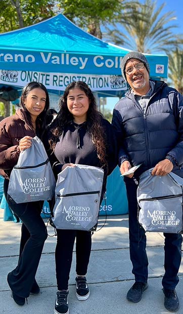 Three students stand side by side holding MVC-branded bags