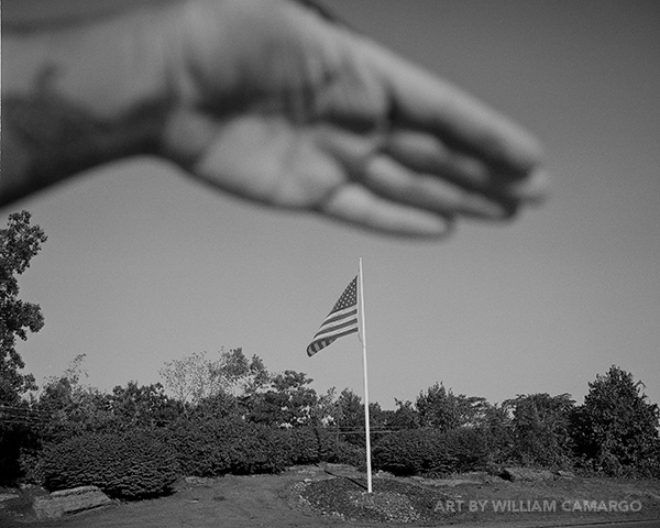 Untitled, a black and white photograph by William Camargo, which shows a blurry hand over an flagpole with the US flag