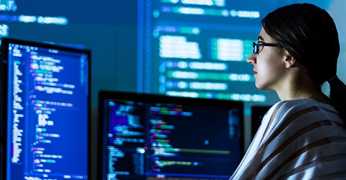 A cybersecurity apprentice sits at a computer with multiple monitors displaying code