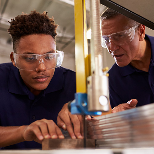 A carpentry apprentice learns how to use a mechanical saw