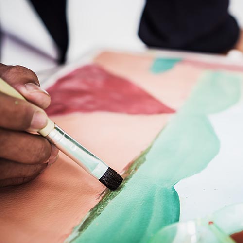 Close-up of a hand holding a paintbrush, painting a landscape with watercolor