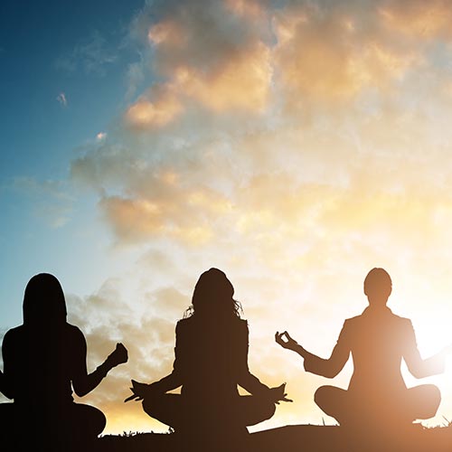 Silhouette of 3 figures meditating against a background of clouds at sunset