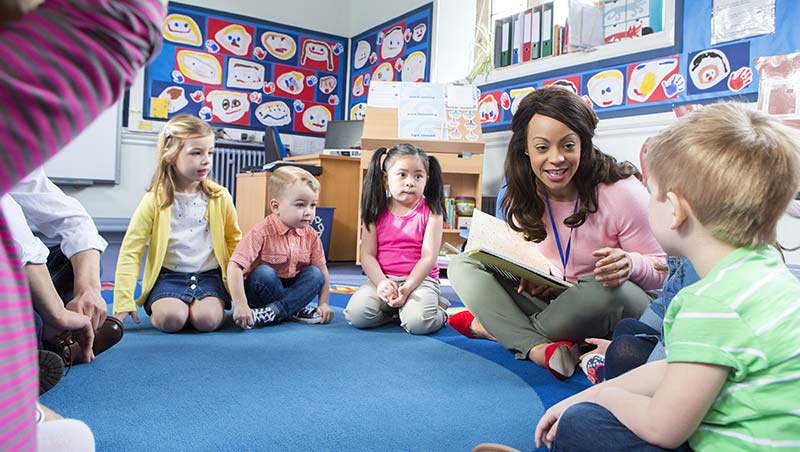 A teacher sits with kids on the floor while reading