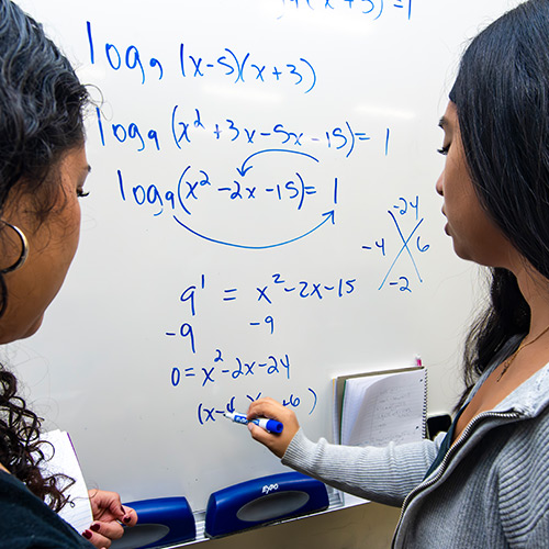 Two students solve math problems on a whiteboard
