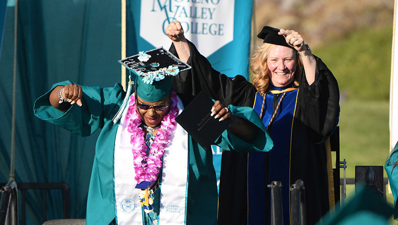 A graduate in regalia dances on stage after receiving degree next to College President, Dr. Robin Steinback
