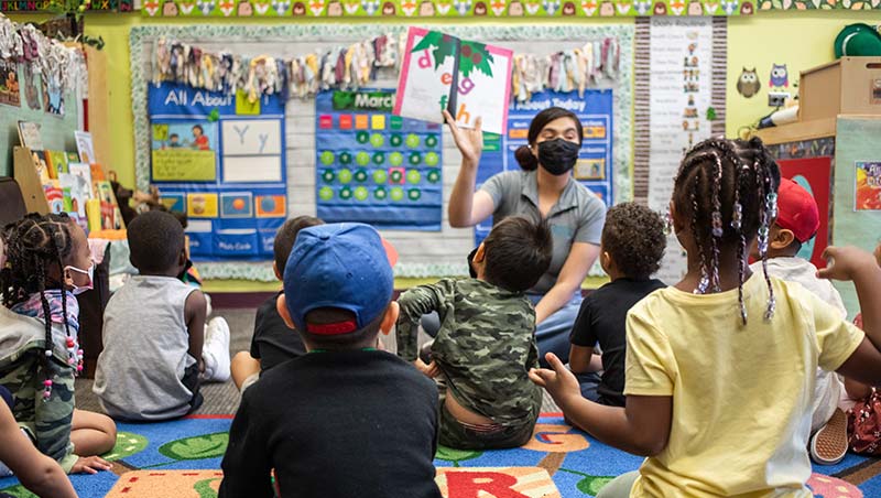 Children sit in the Early Childhood Education Center during story time while a teacher holds up a picture book