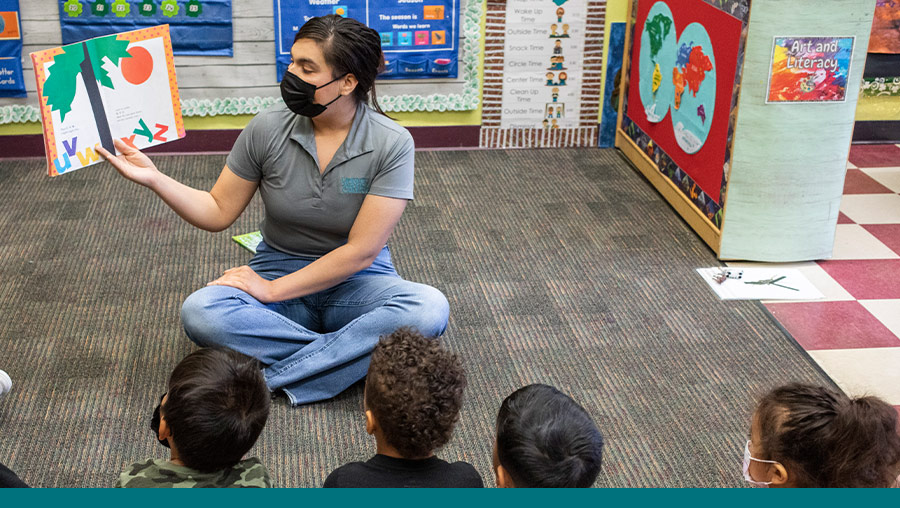 An MVC early childhood instructor holds up and reads a picture book to a group of young children