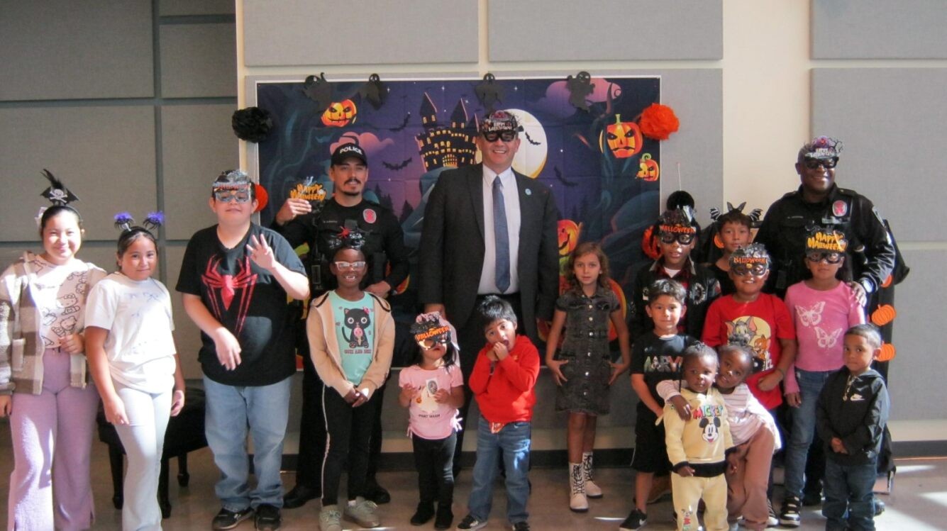 President Besikof stands with group of children in halloween costumes