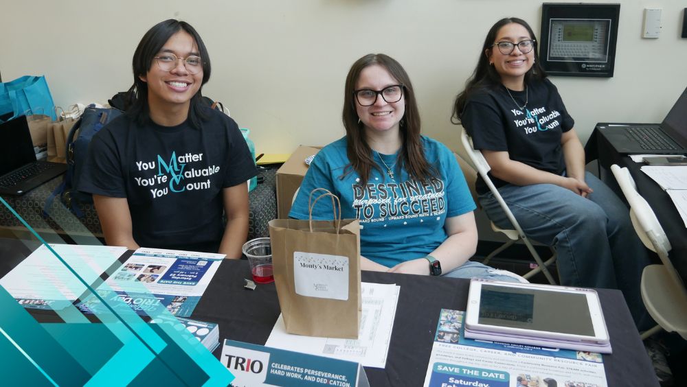 Three students smile while tabling during a TRIO-hosting community event