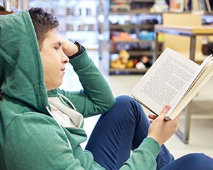 A student reads a book while sitting on the ground
