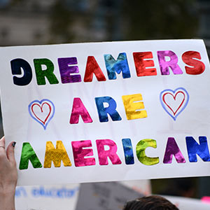 A protester holds up a sign stating Dreamers are American in rainbow lettering