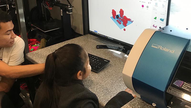 An elementary school student uses a computer to set up the iMake Mobile vinyl printer