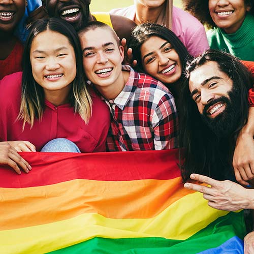 A group of diverse students sit on the grass with pride flag on their lap