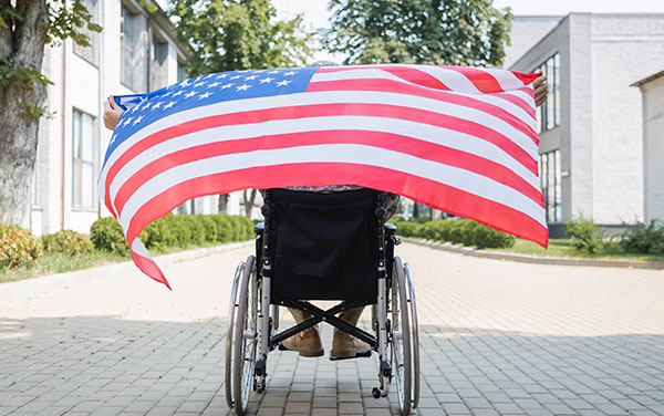 A veteran in a wheel chair unfurls a US flag behind them